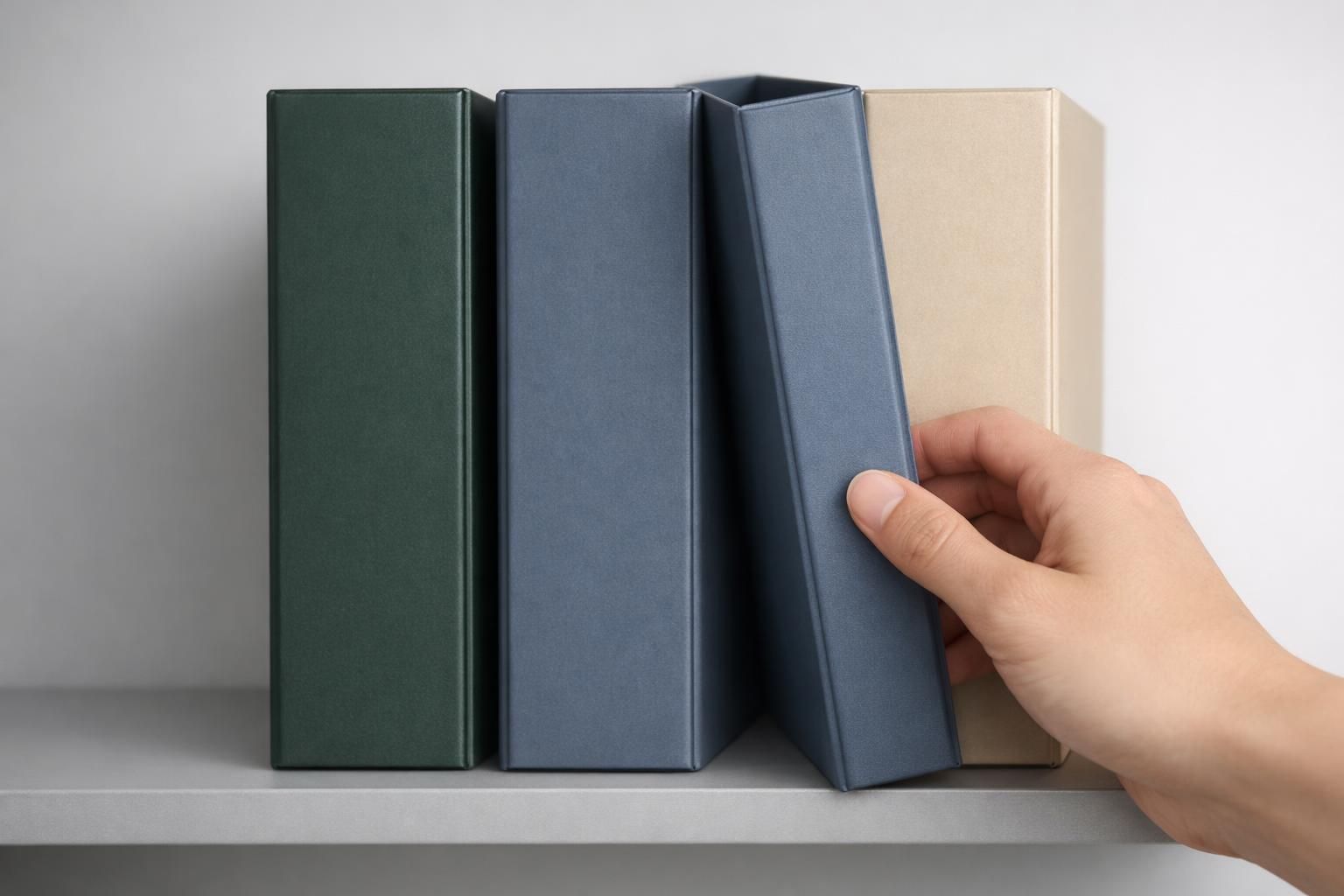 Main sortant un classeur bleu parmi des classeurs de couleurs différentes