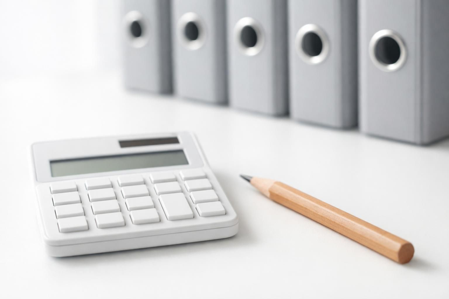 Calculatrice, crayon et classeurs gris alignés sur un bureau blanc